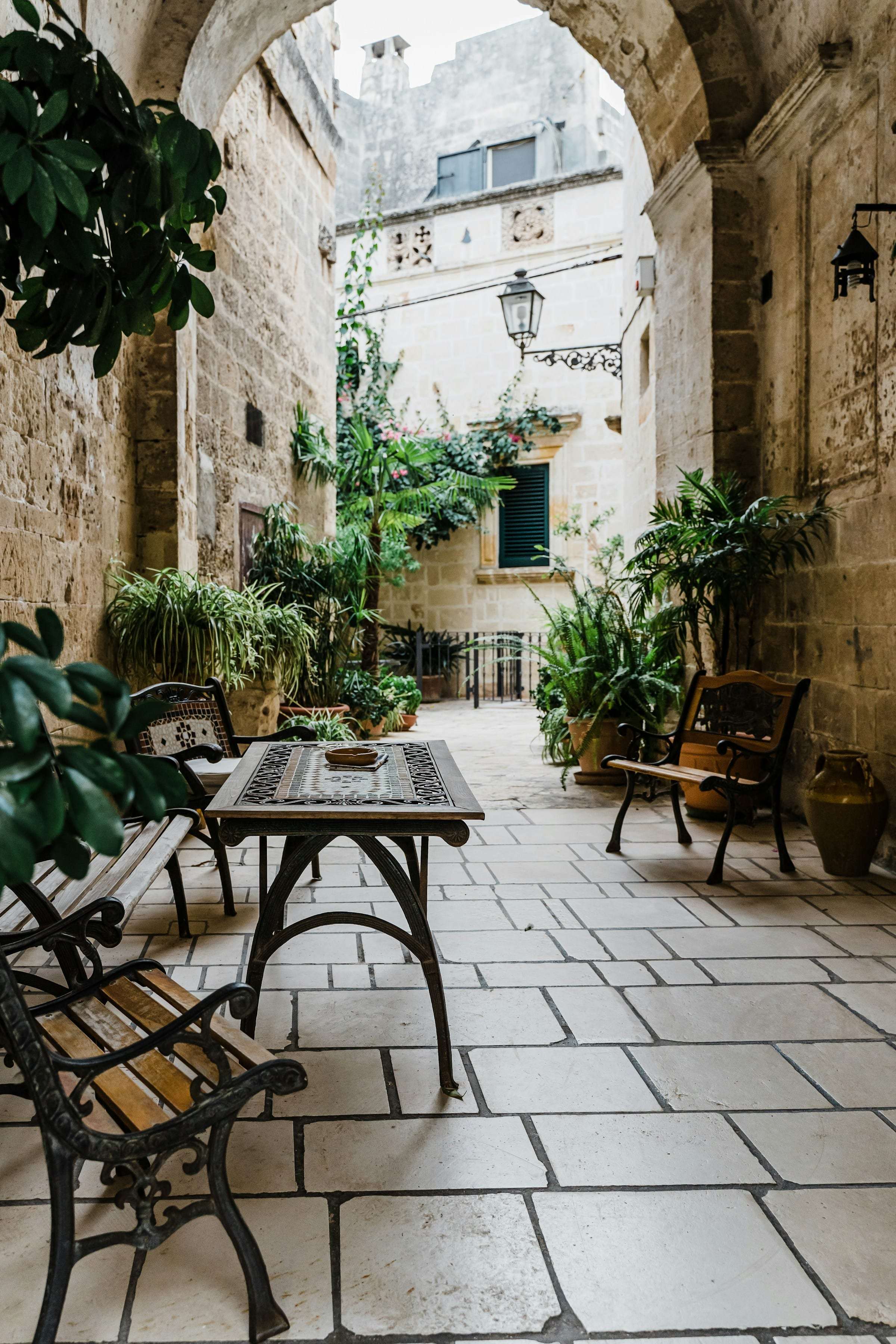 A stone courtyard under an archway, a table and chairs set among the plants.