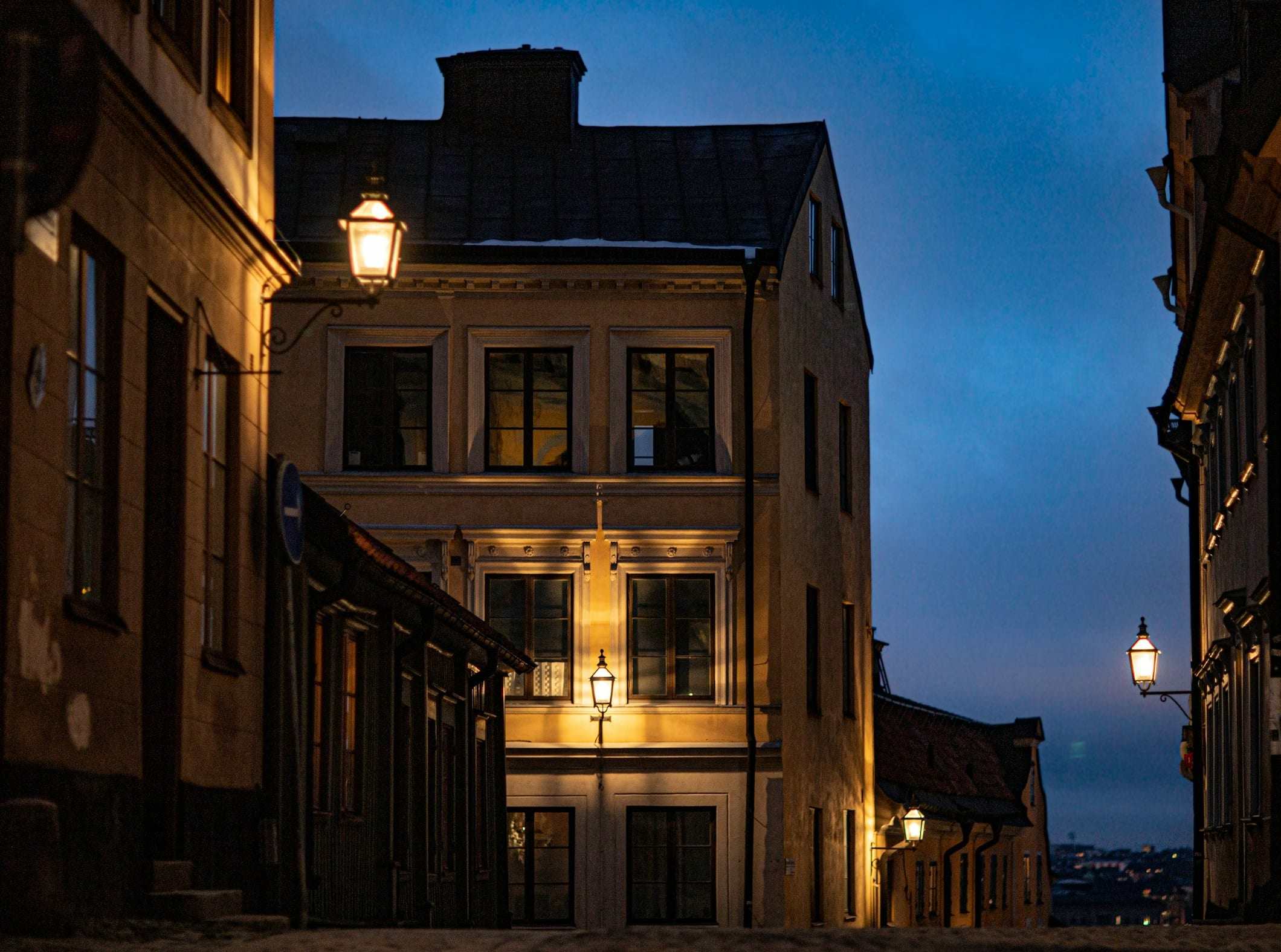 A row of old townhouses at blue hour, lamplight falling on the street below.