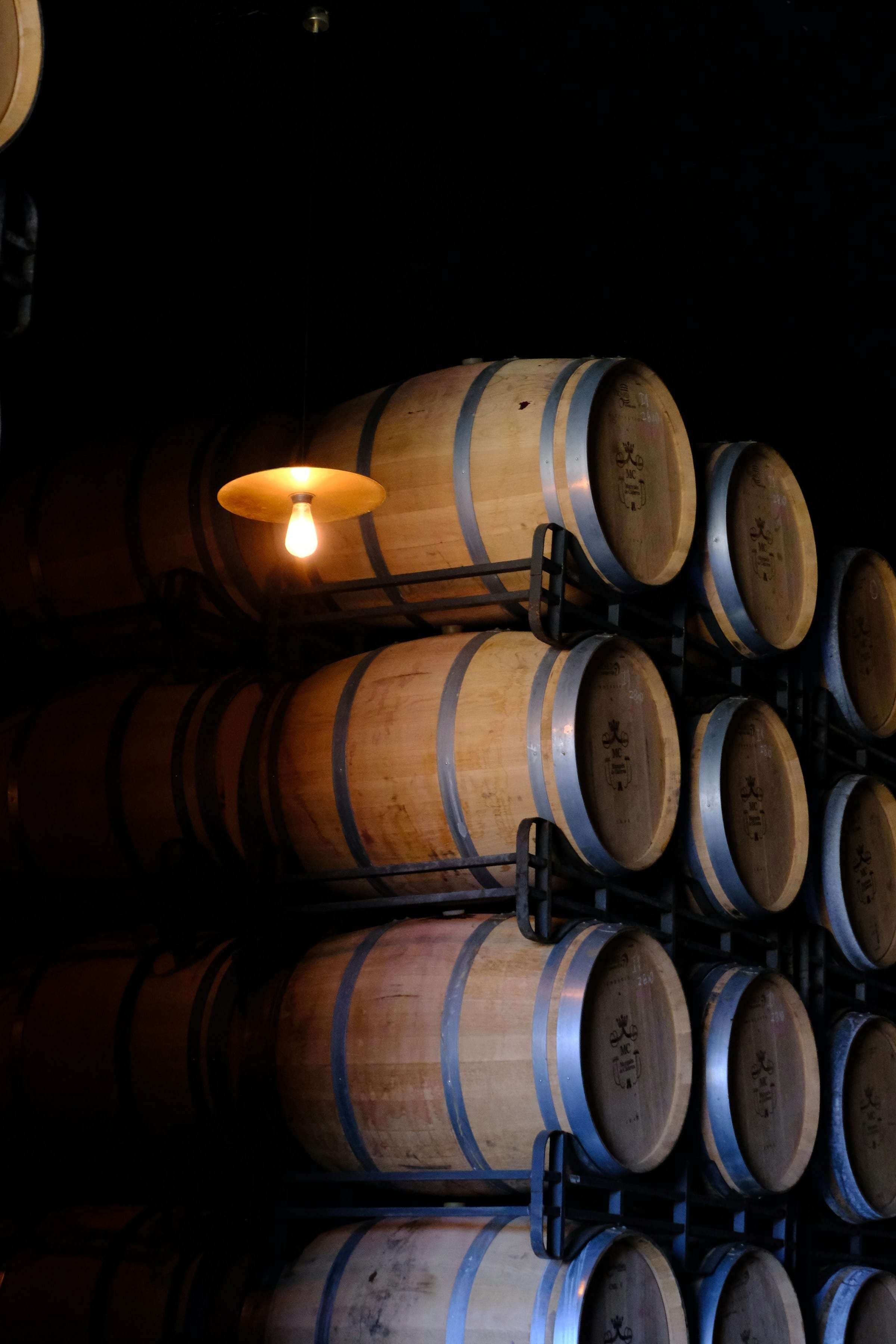 Oak barrels stacked in a dark cellar under a single hanging lamp.