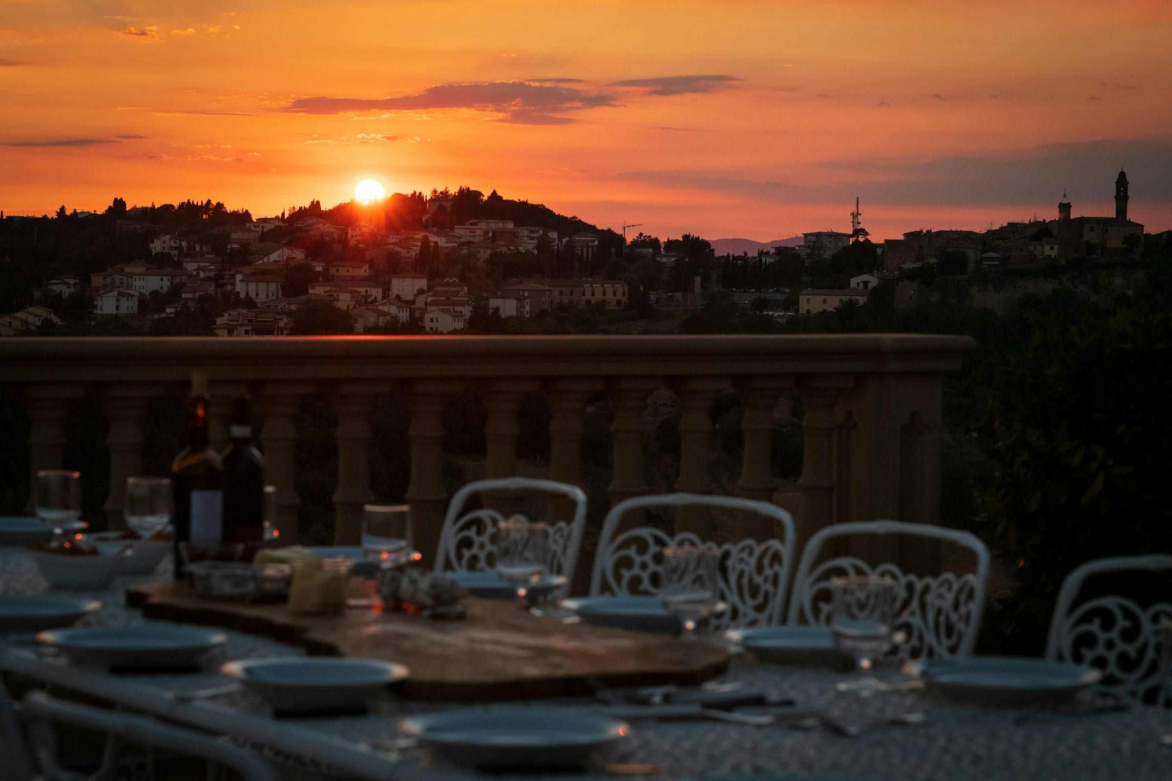 A long table laid on a veranda, the sun going down over the hills beyond the balustrade.